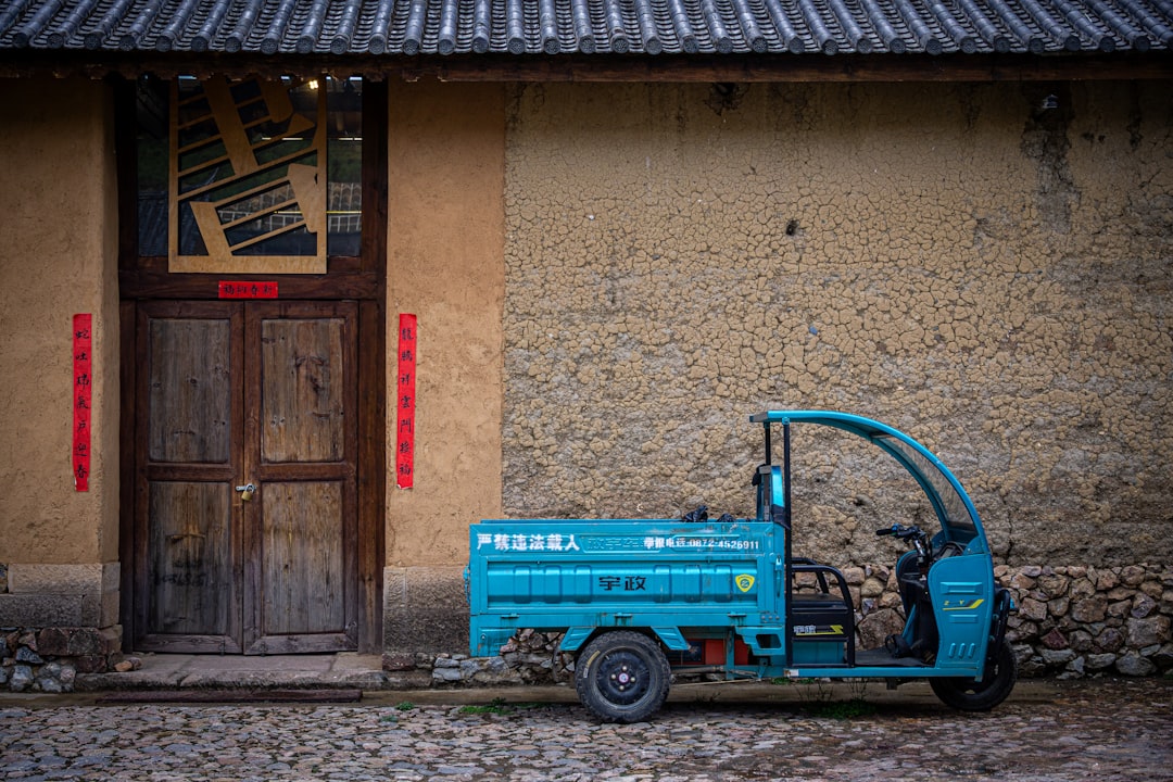 a-blue-tricycle-is-parked-beside-a-building-9ngxuglnlgy